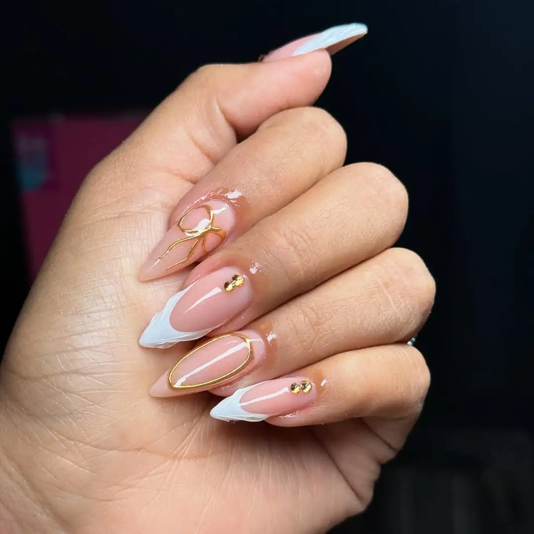 almond nails with gold bow detailing, white french tips, and small gold rhinestones.