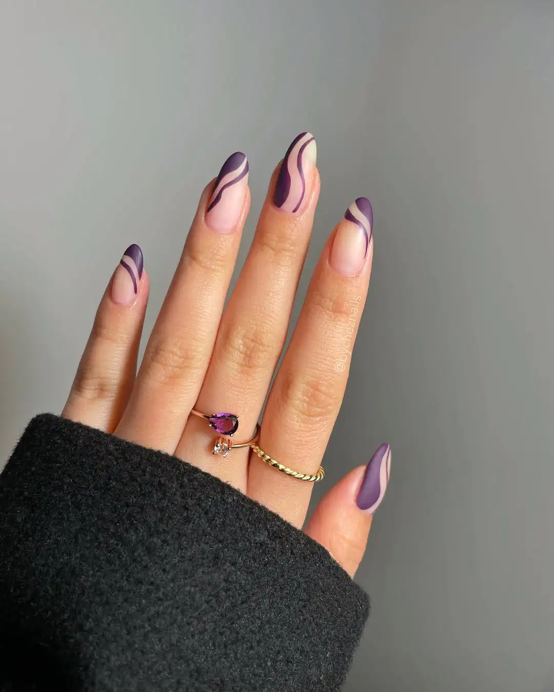 almond shaped nails featuring deep purple wavy swirls on a neutral base with rings