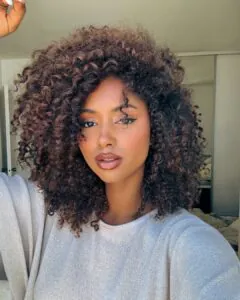 woman with voluminous natural brown curls and warm glowing makeup