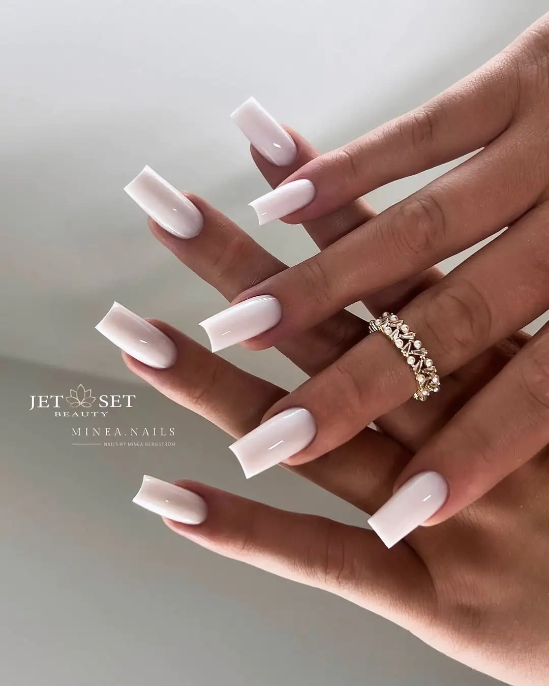 long square milky white gel nails on a hand with a pearl ring