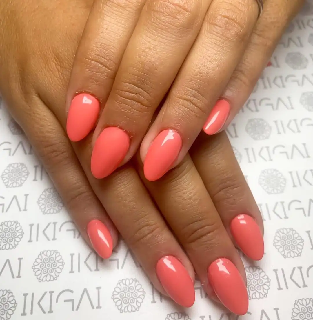 glossy coral pink almond nails displayed over a branded white background