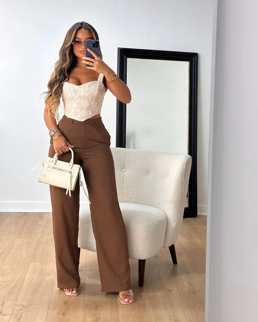 woman wearing floral corset top and brown wide leg trousers holding white handbag