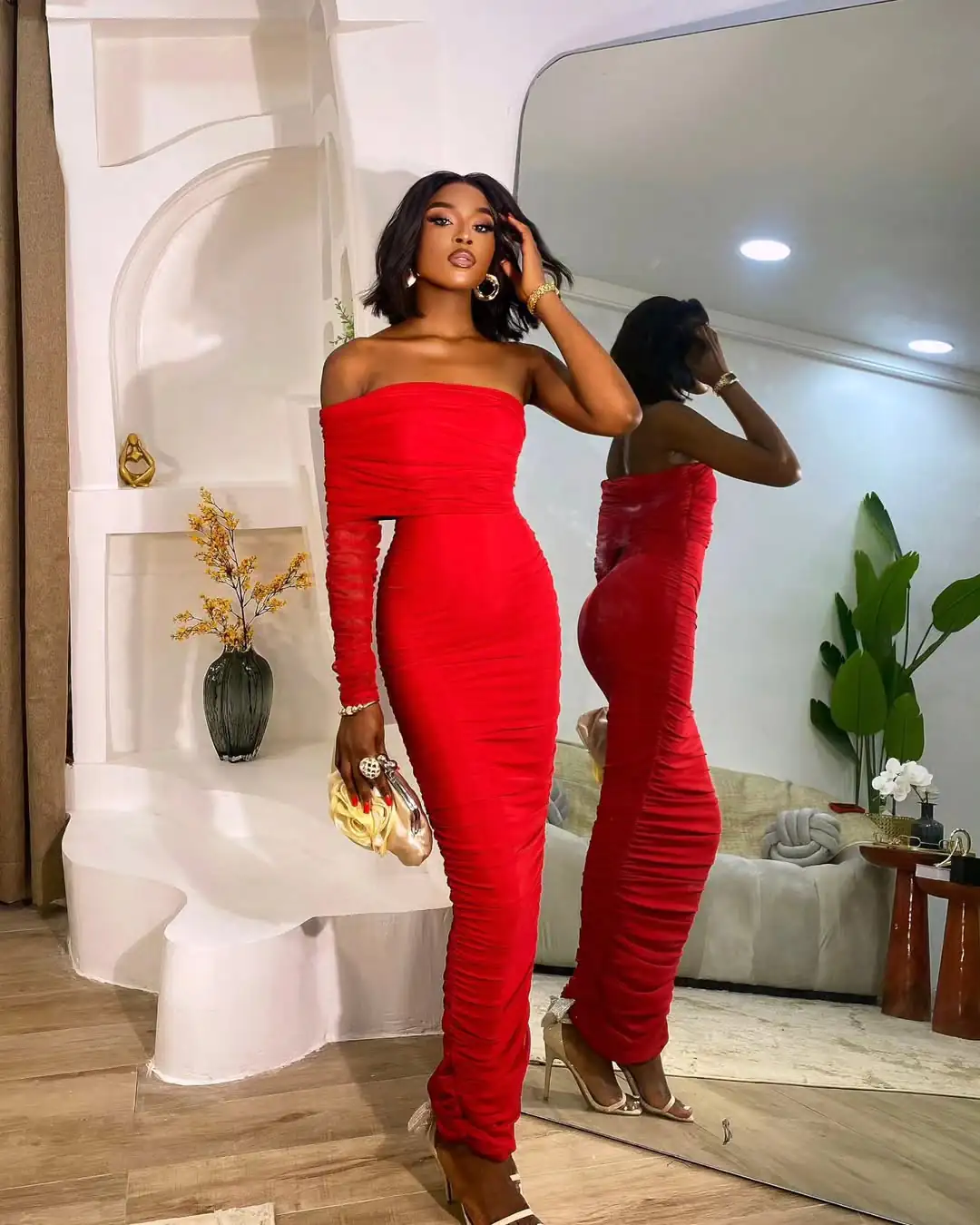 woman wearing vibrant red off the shoulder ruched maxi dress with gold clutch