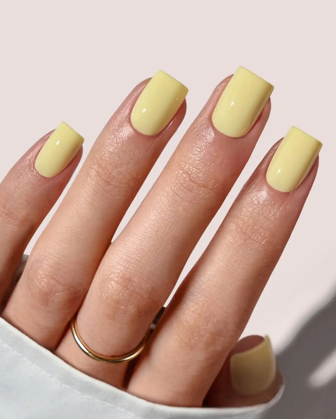 square shaped lemon yellow gel nails on a hand wearing a gold ring