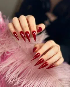 glossy dark red stiletto nails resting against a pink feathered background