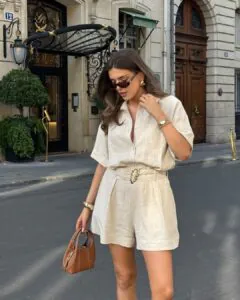 woman wearing a beige linen short set and dark sunglasses on a city street.