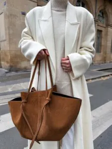 woman wearing oversized white winter coat and holding a brown suede tote bag.
