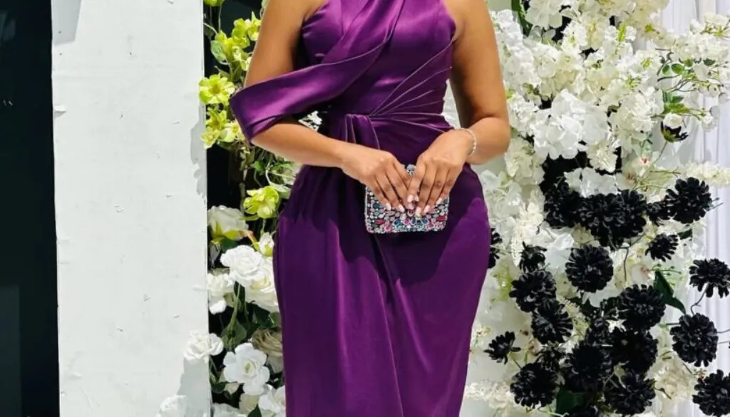 woman in high neck purple satin gown standing before a white floral backdrop