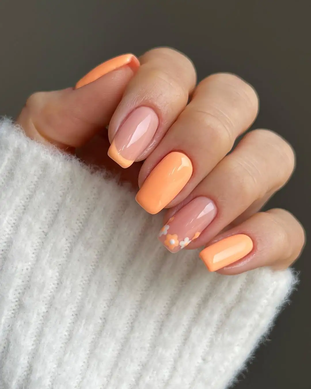square peach nails with matching french tips and small white and orange floral accents