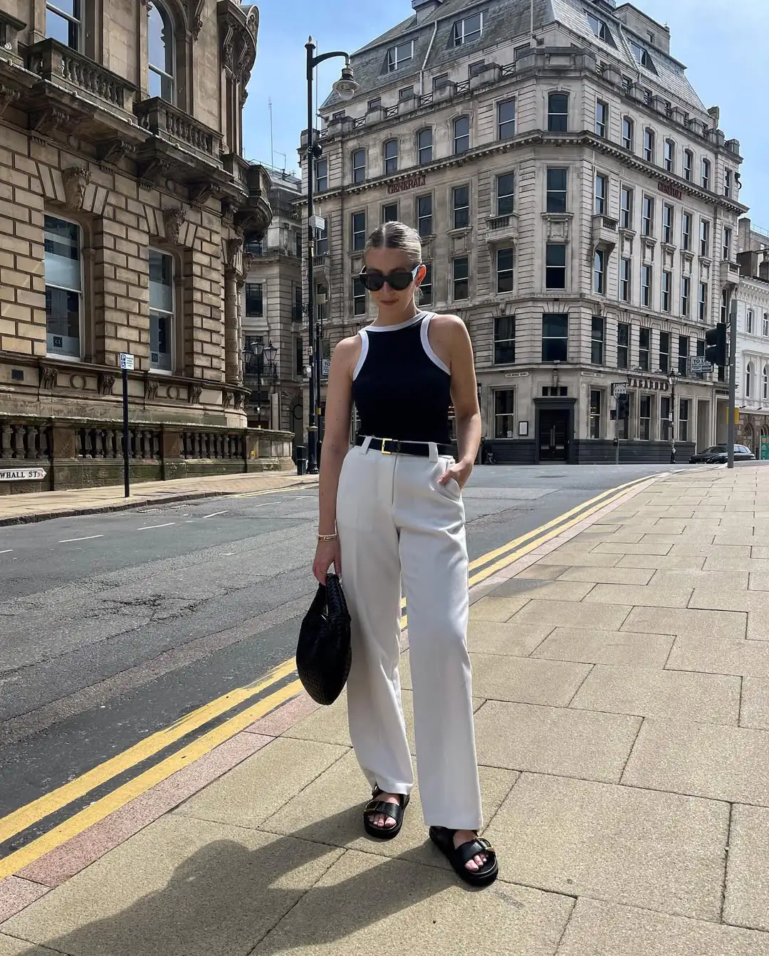 woman in black sleeveless top and white trousers walking through historic city street