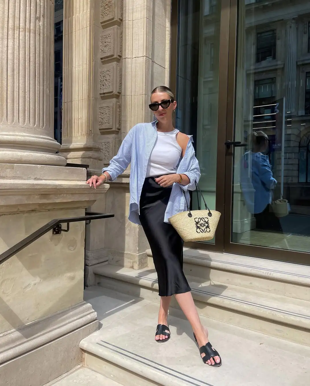 woman wearing blue striped shirt over black satin skirt standing on stone steps