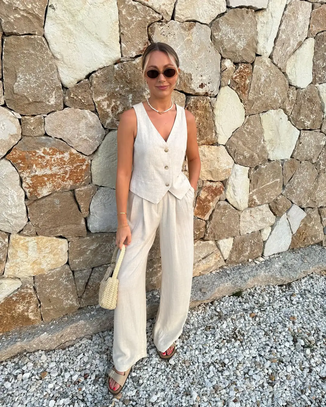 woman wearing beige linen vest and matching wide leg trousers against stone wall