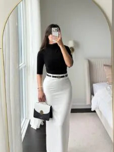 woman in black mock neck top and white maxi skirt taking a mirror selfie.