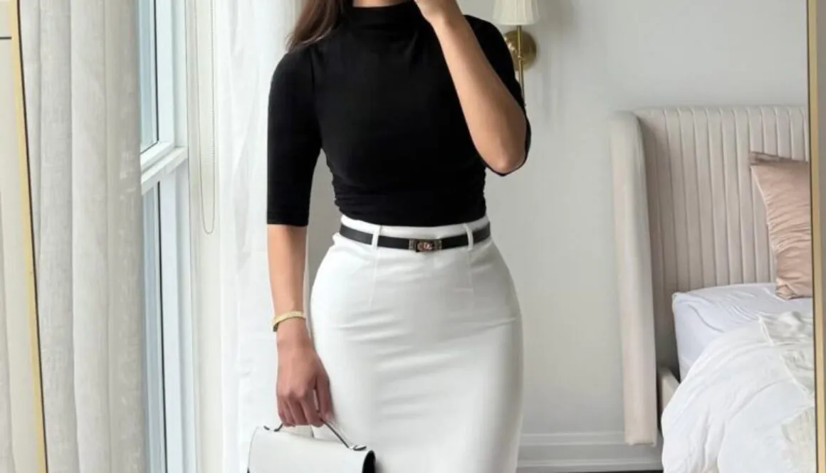 woman in black mock neck top and white maxi skirt taking a mirror selfie.