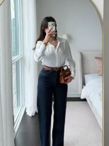 woman wearing white button-down silk shirt and dark denim jeans with a brown belt.