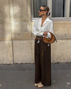 woman wearing a white silk blouse and chocolate brown wide-leg trousers with a suede handbag.