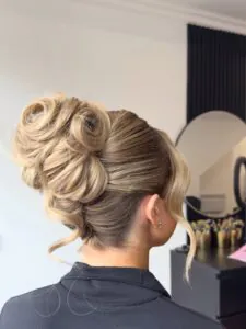 side view of woman with voluminous blonde wedding guest updo and face framing strands