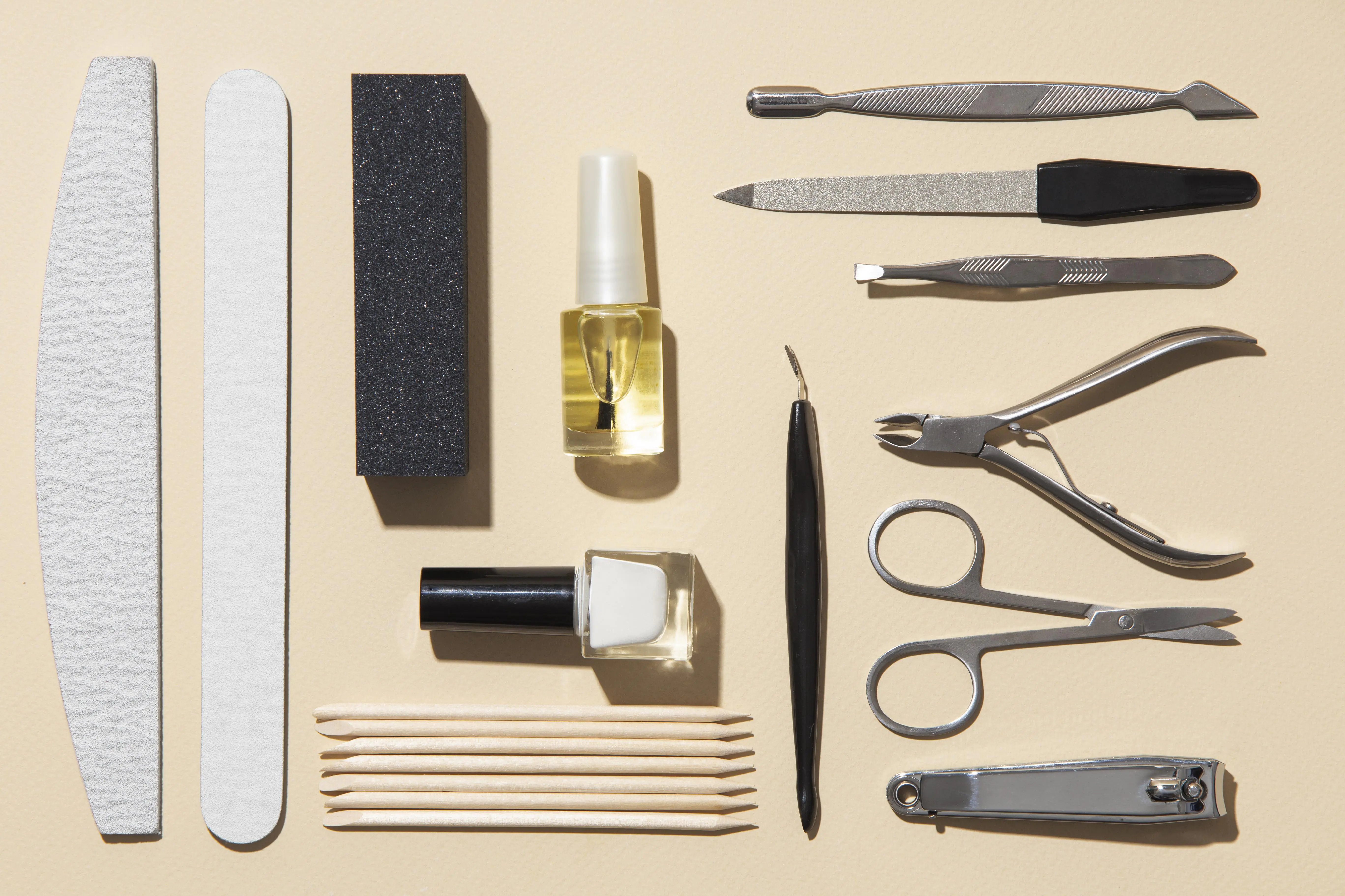 neat arrangement of professional manicure tools, nail polish, files, and cuticle sticks on beige background