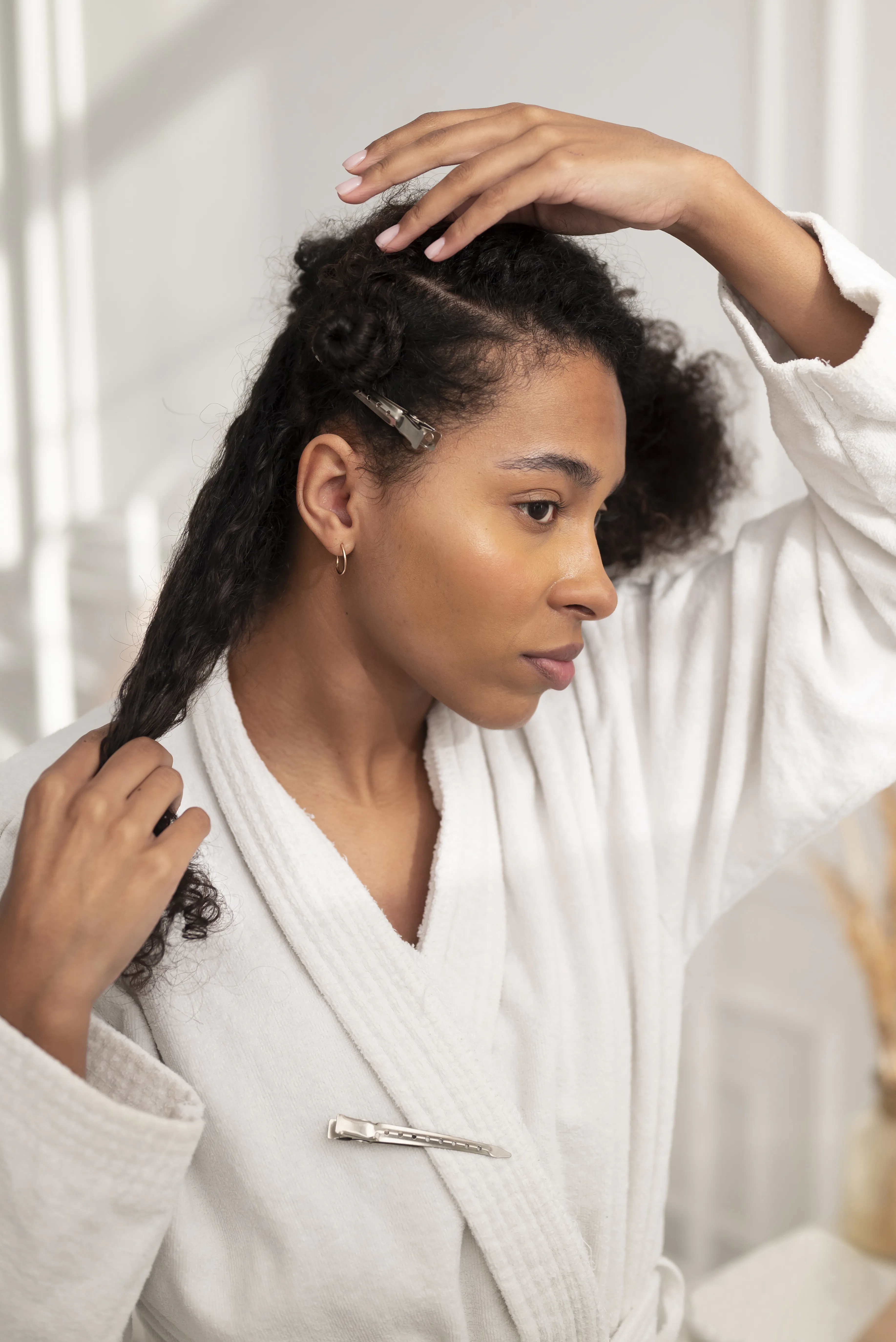 person in a white robe sectioning and styling their curly hair with clips