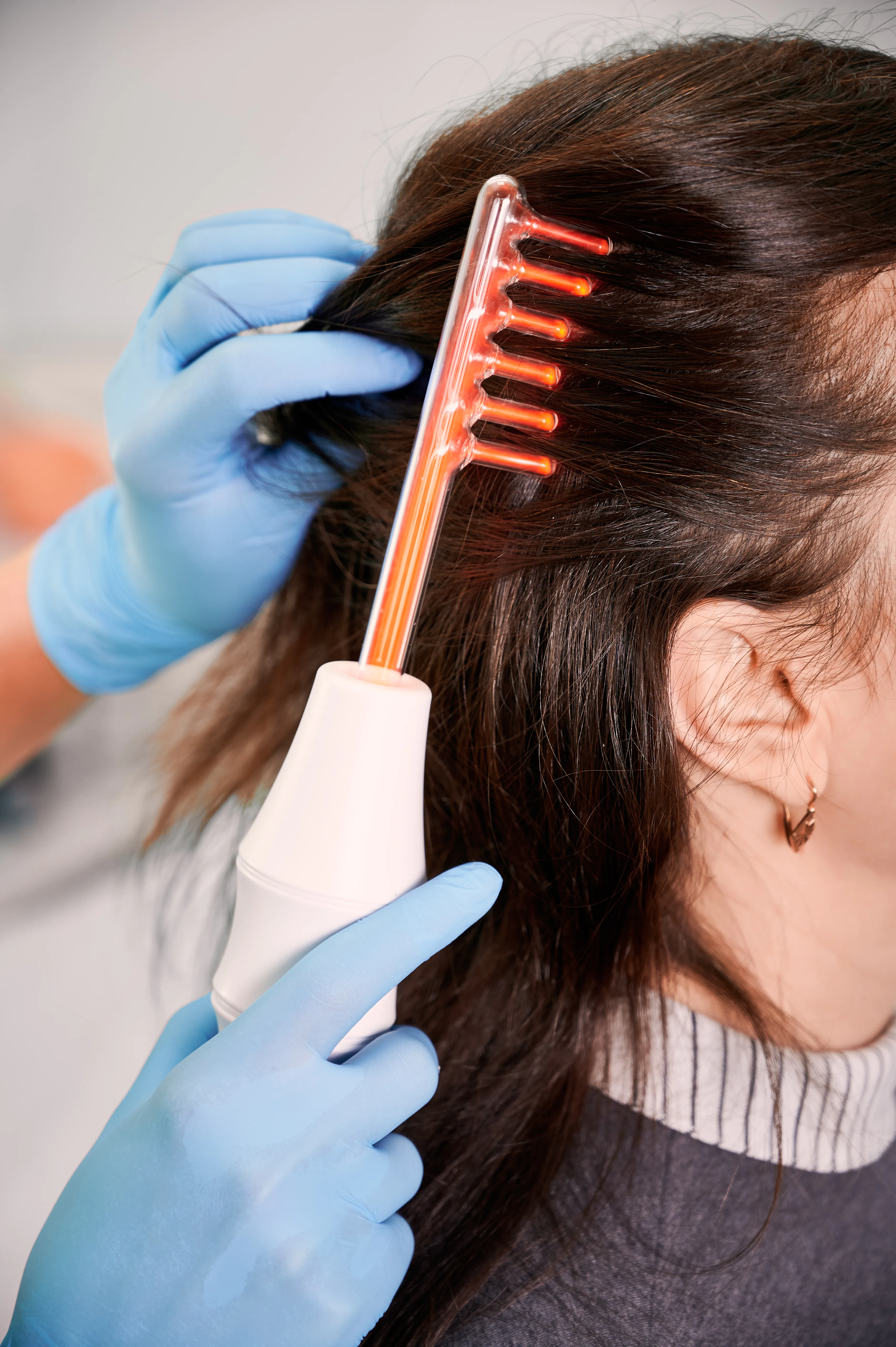 specialist applying a glowing high frequency glass comb treatment to a person's scalp