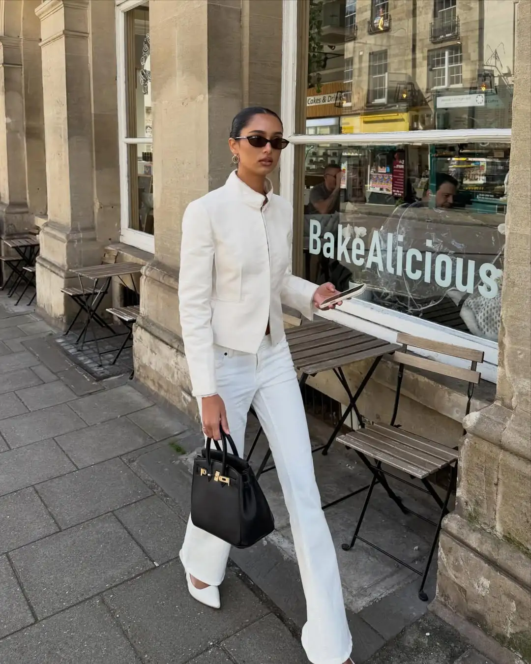 woman in white jacket and matching jeans walking past a cafe storefront