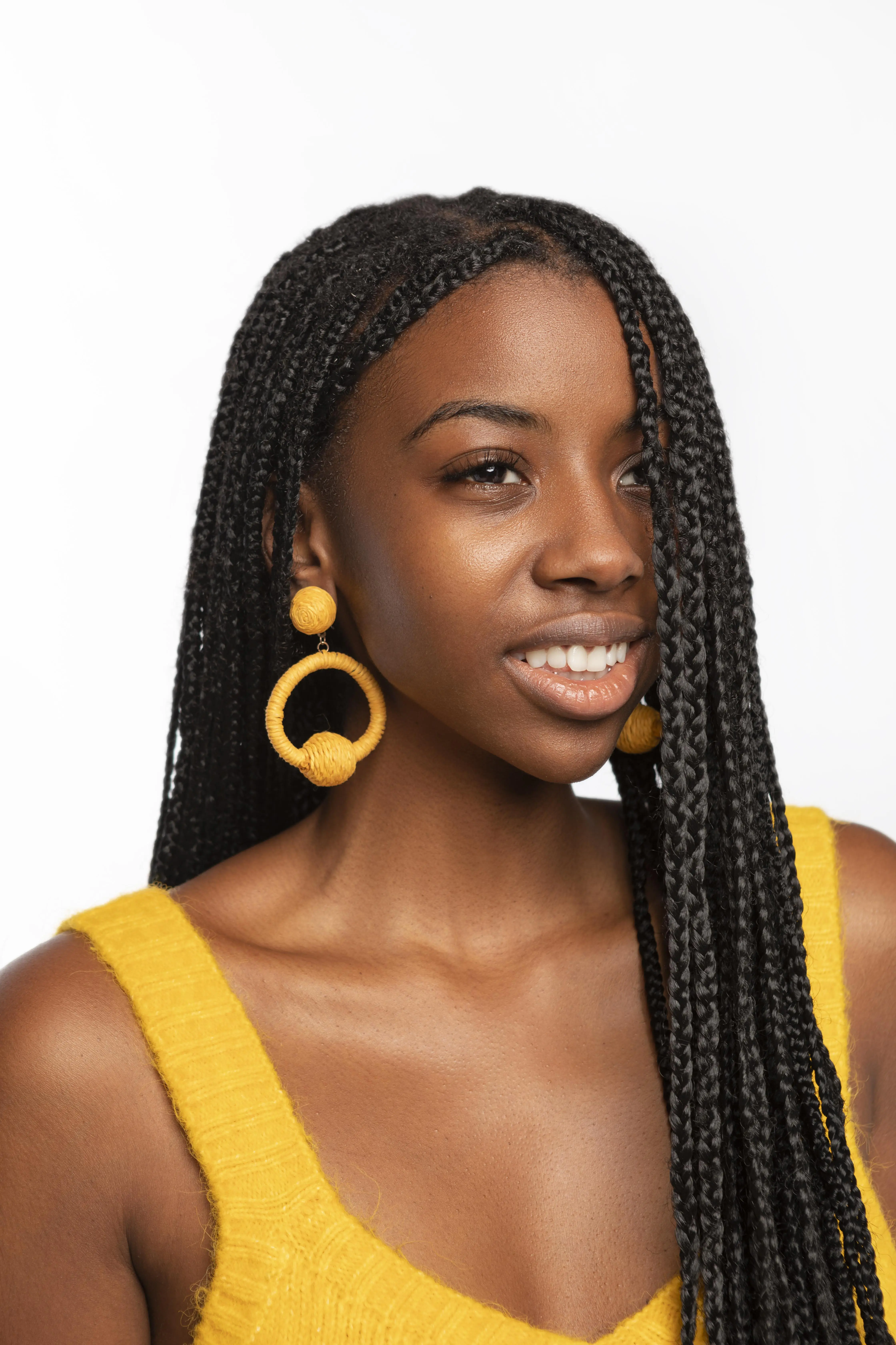 woman with long black box braids wearing large yellow hoop earrings and smiling