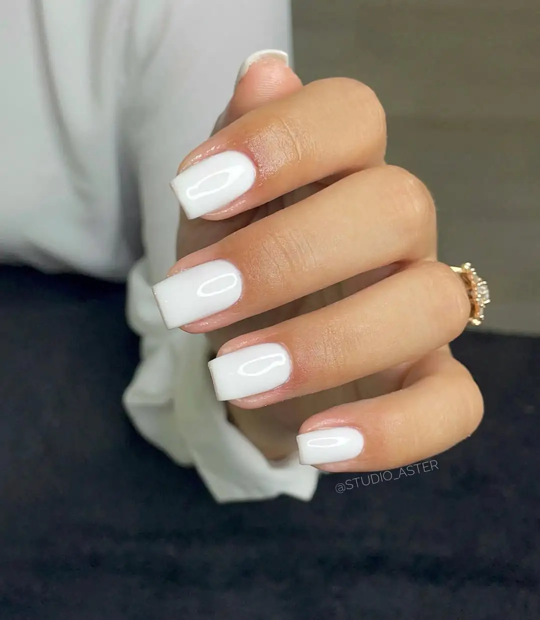 short square glossy white nails on a hand with a gold ring