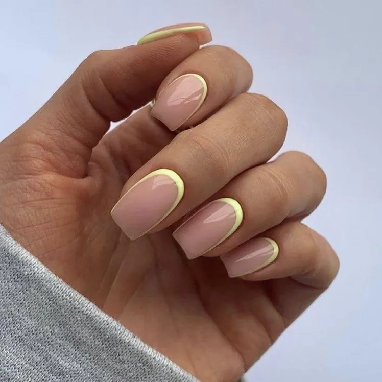 square nude nails with thin pale yellow french tips on the cuticle line