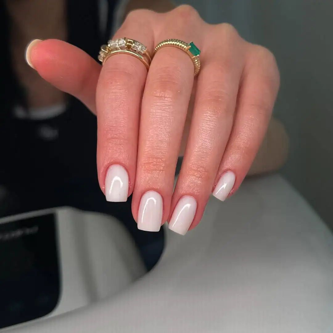 short square milky white nails featuring gold and emerald green rings