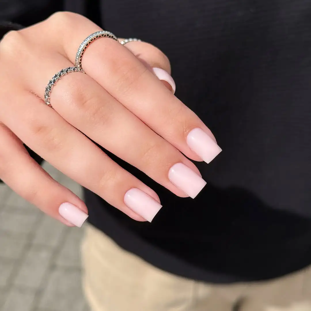 short square light pink nails on a hand wearing silver rings