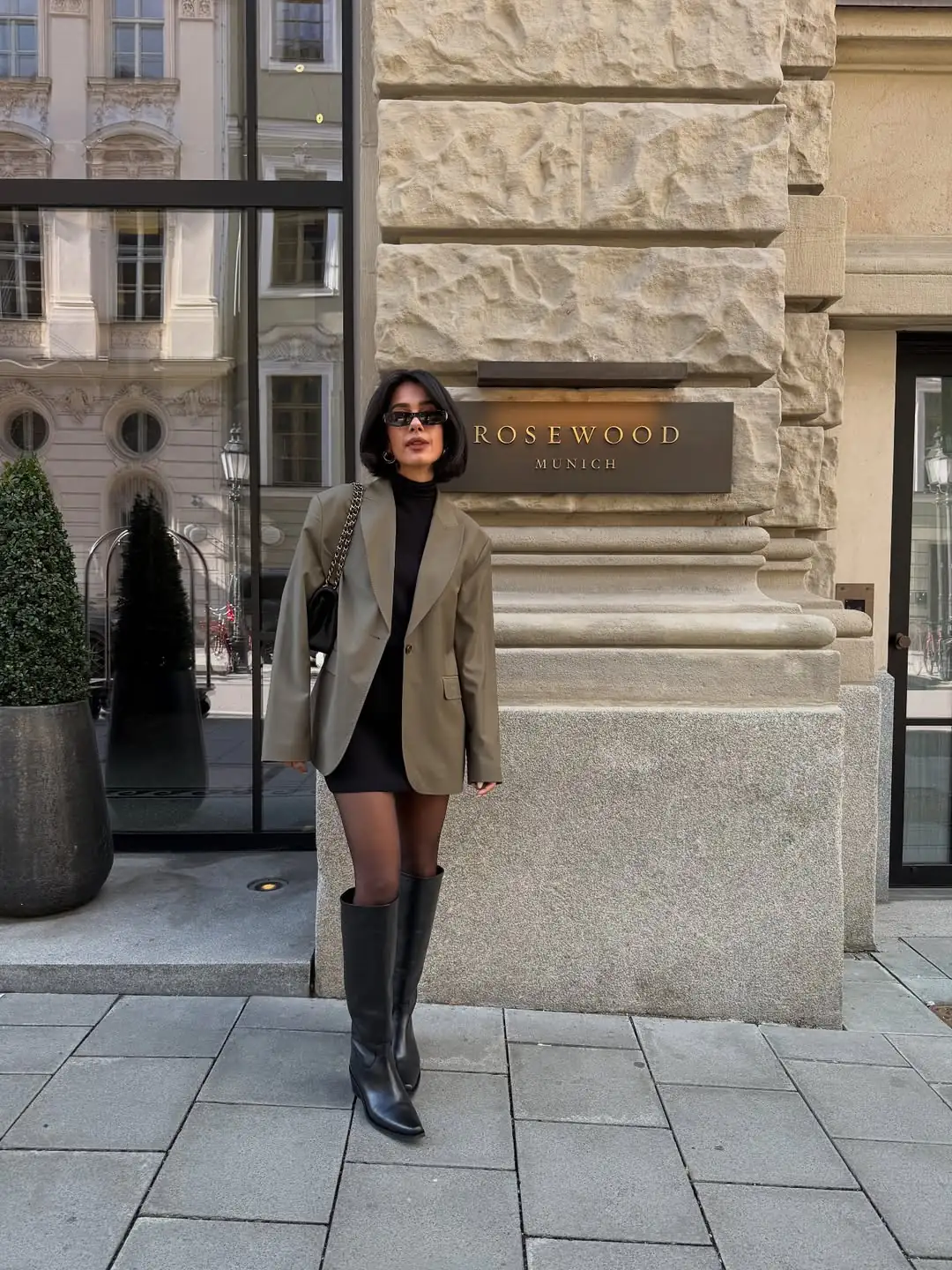 woman wearing olive blazer over black mini dress and knee high boots