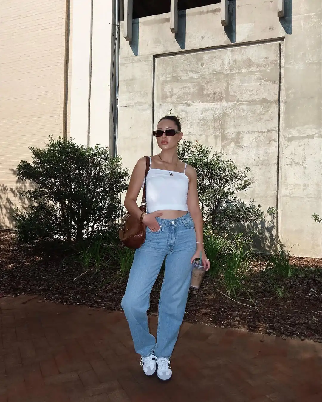 woman in white crop top and blue jeans standing near green bushes