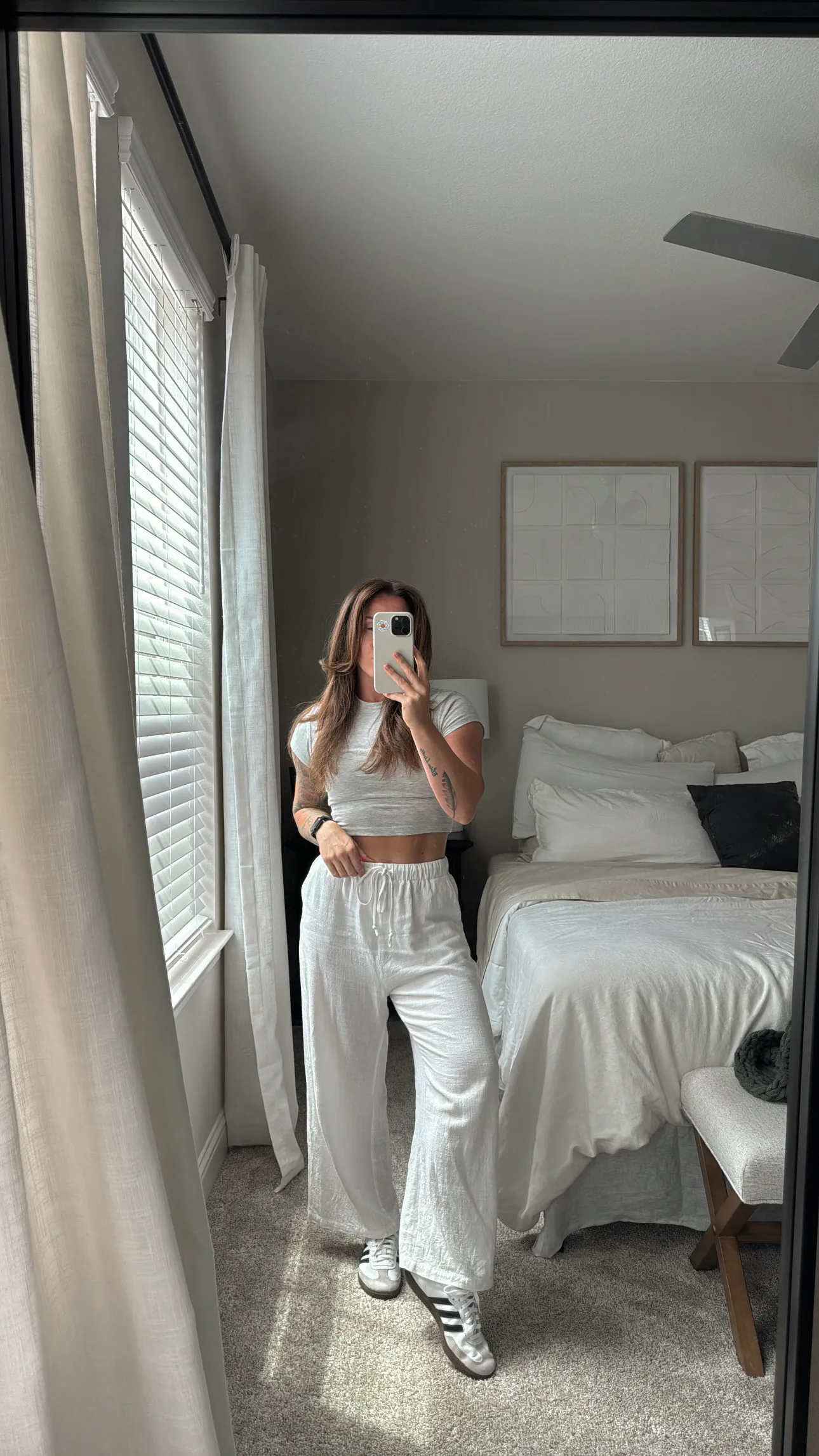 woman in white linen lounge set taking mirror selfie in bedroom