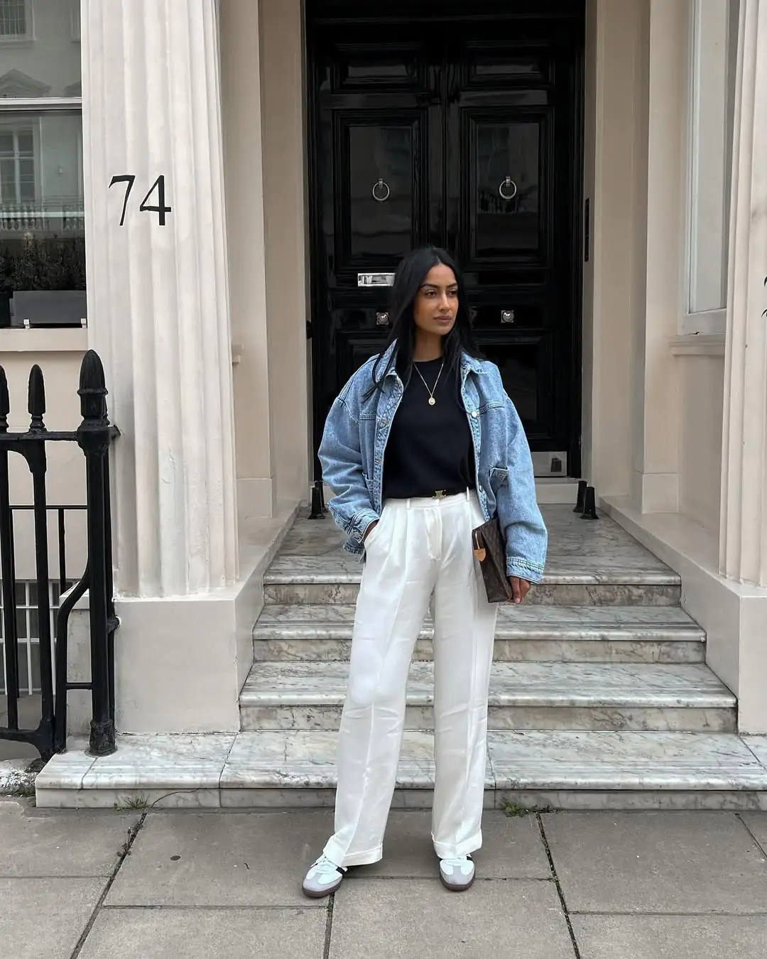 woman in denim jacket and white trousers standing before black front door