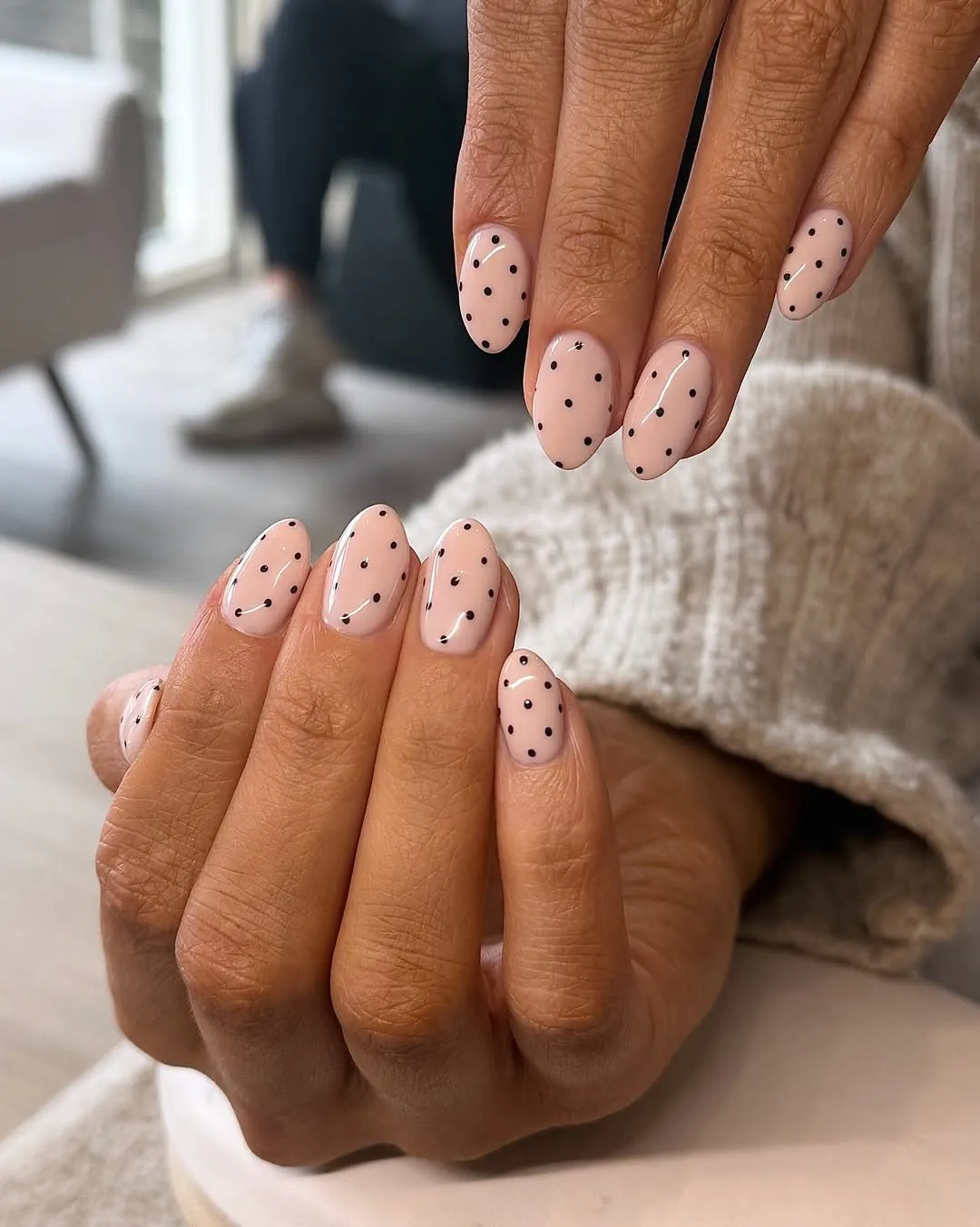 oval gel nails painted in a nude pink color with minimalist black polka dots