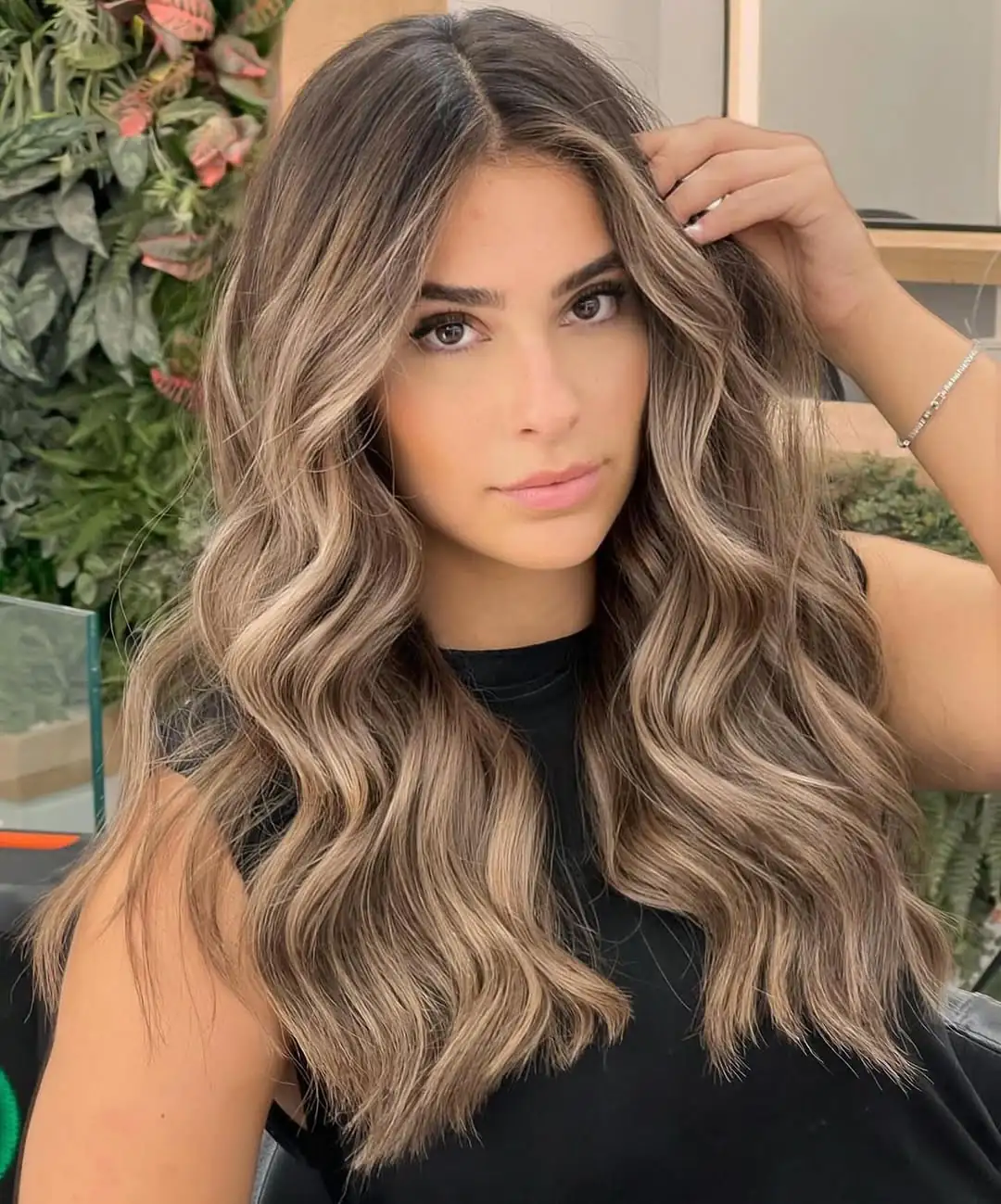 woman with long ash brown hair and blonde balayage styled in loose polished waves