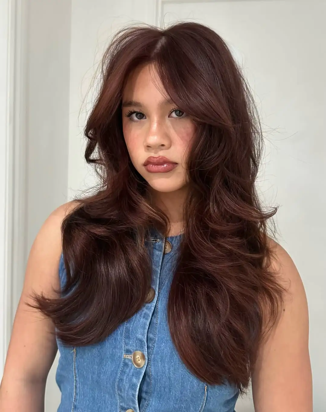 woman with long auburn red hair styled in voluminous butterfly layers and curtain bangs
