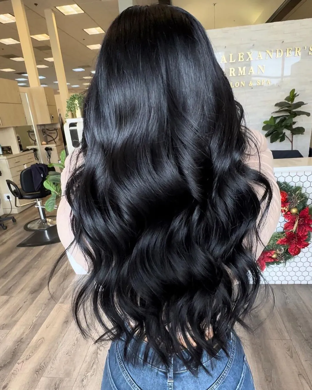 back view of a woman with long shiny wavy black hair in a salon