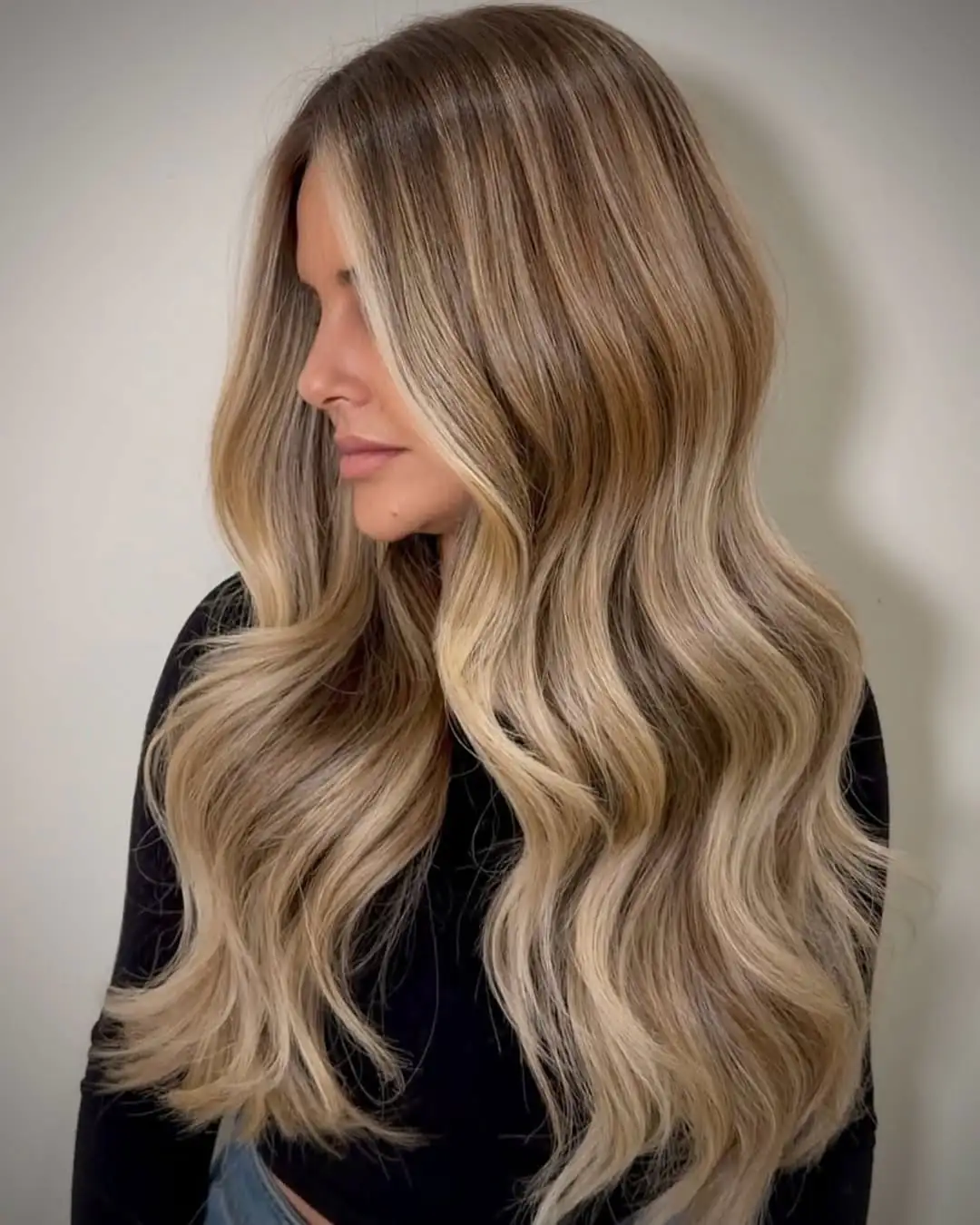 side profile of a woman with long wavy blonde hair and dark roots