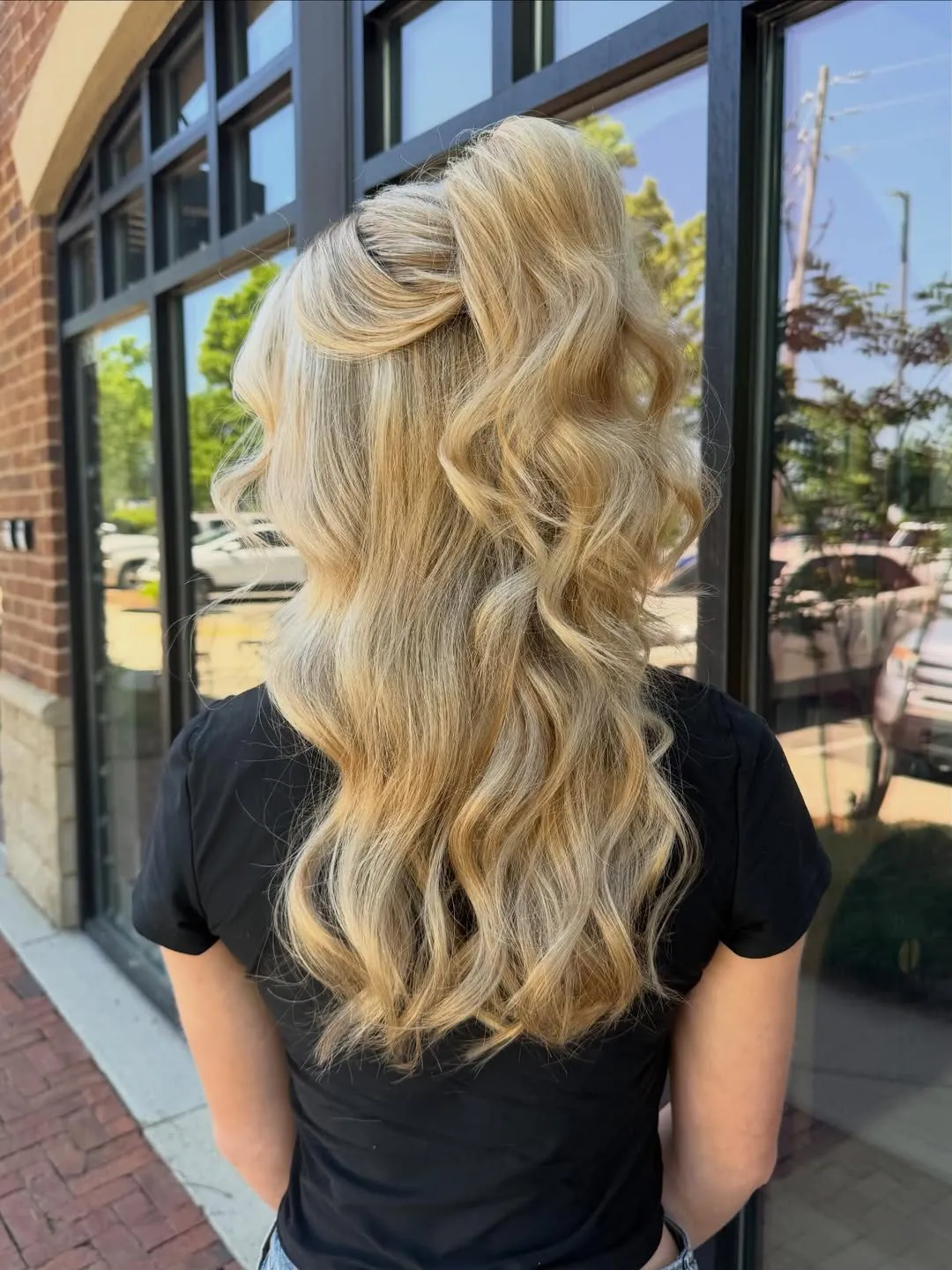 blonde woman with long wavy hair in a high half-up ponytail standing outdoors.
