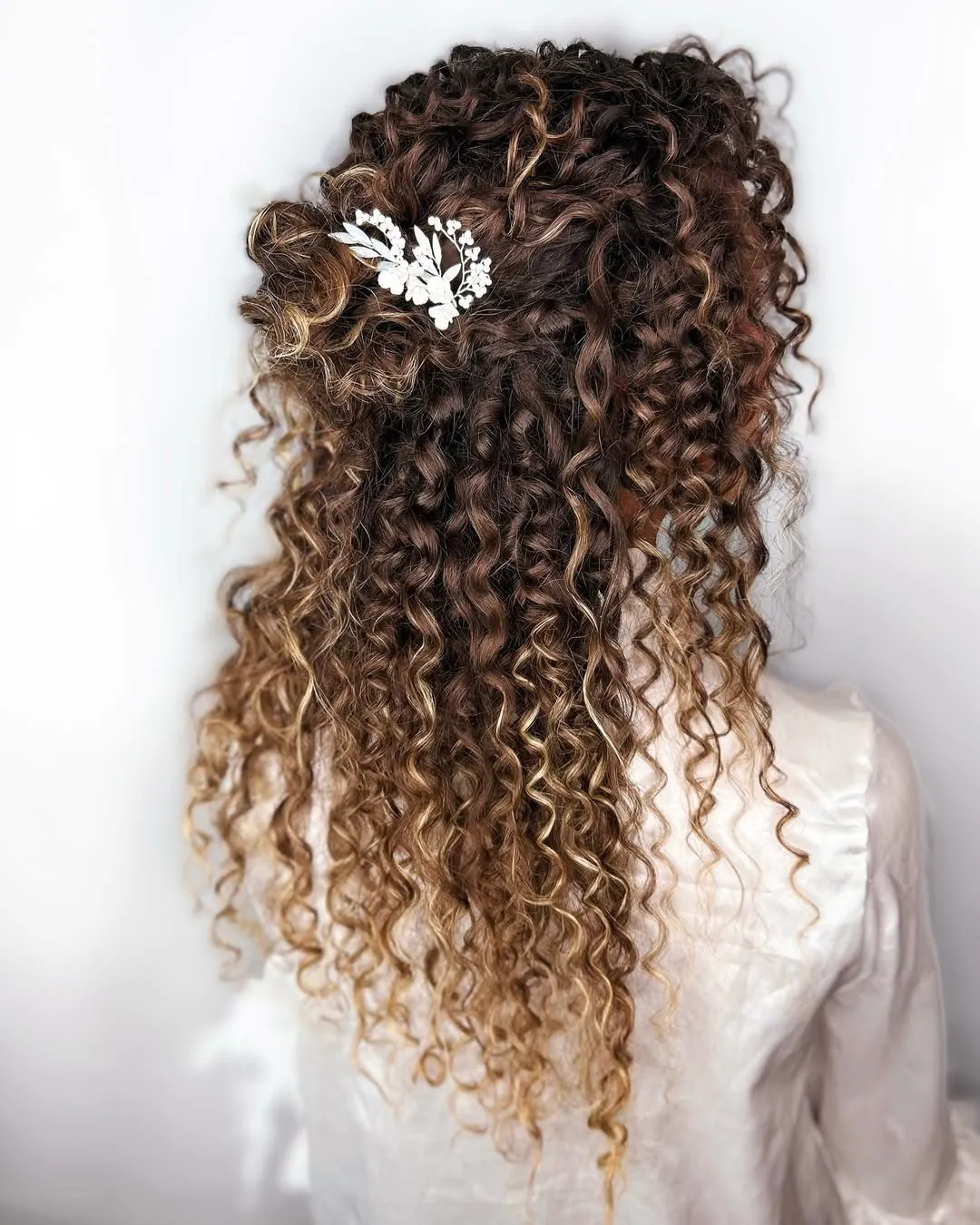 voluminous tight curls in a half-up hairstyle adorned with a white floral hair clip.