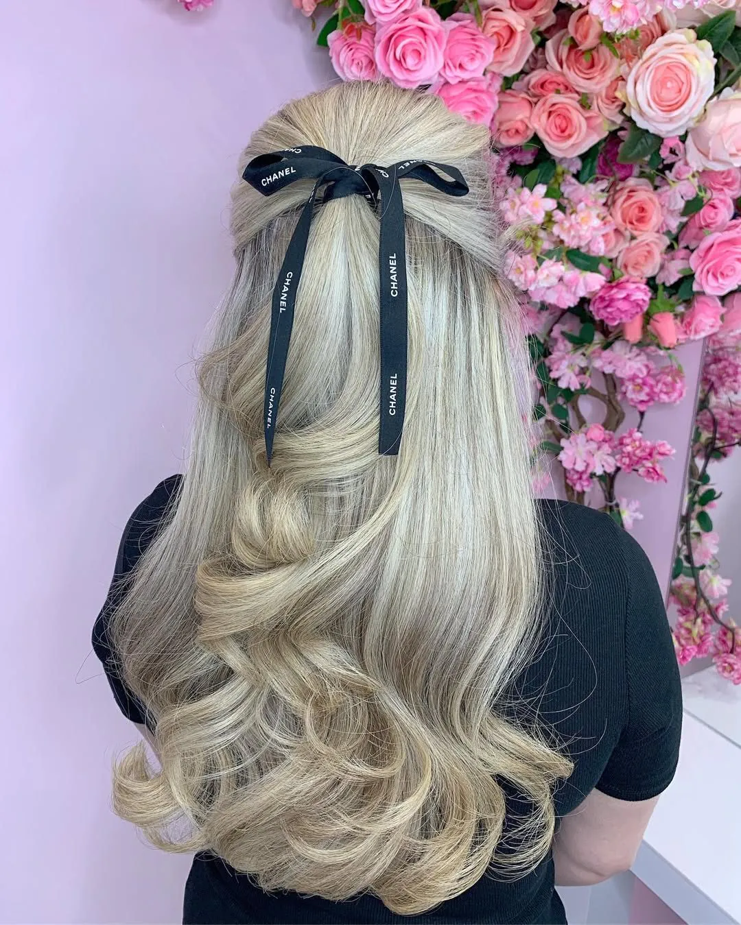 long blonde wavy hair in a half-up style tied with a black designer ribbon bow.