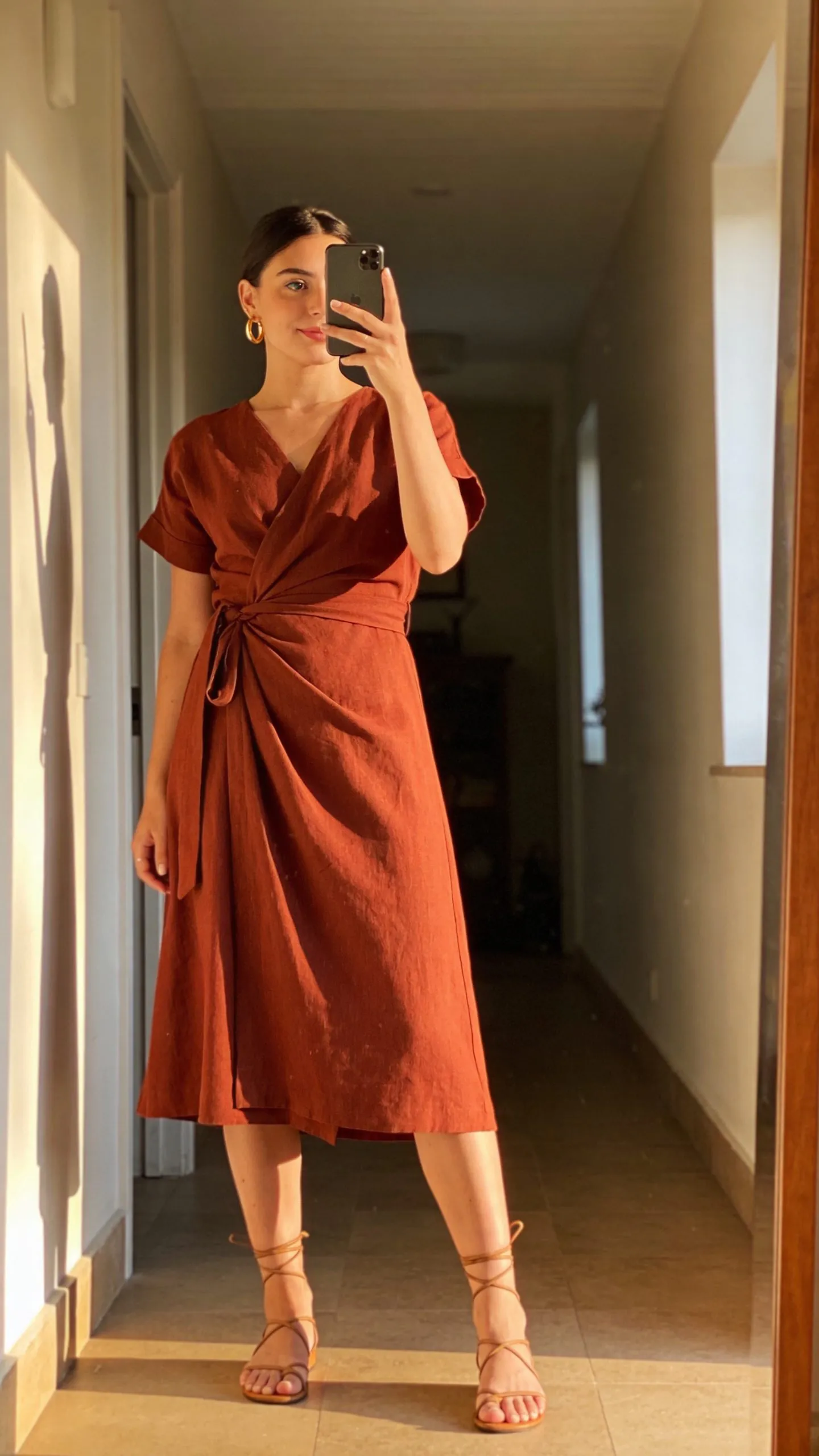 woman in burnt orange wrap dress and lace-up sandals taking a mirror selfie