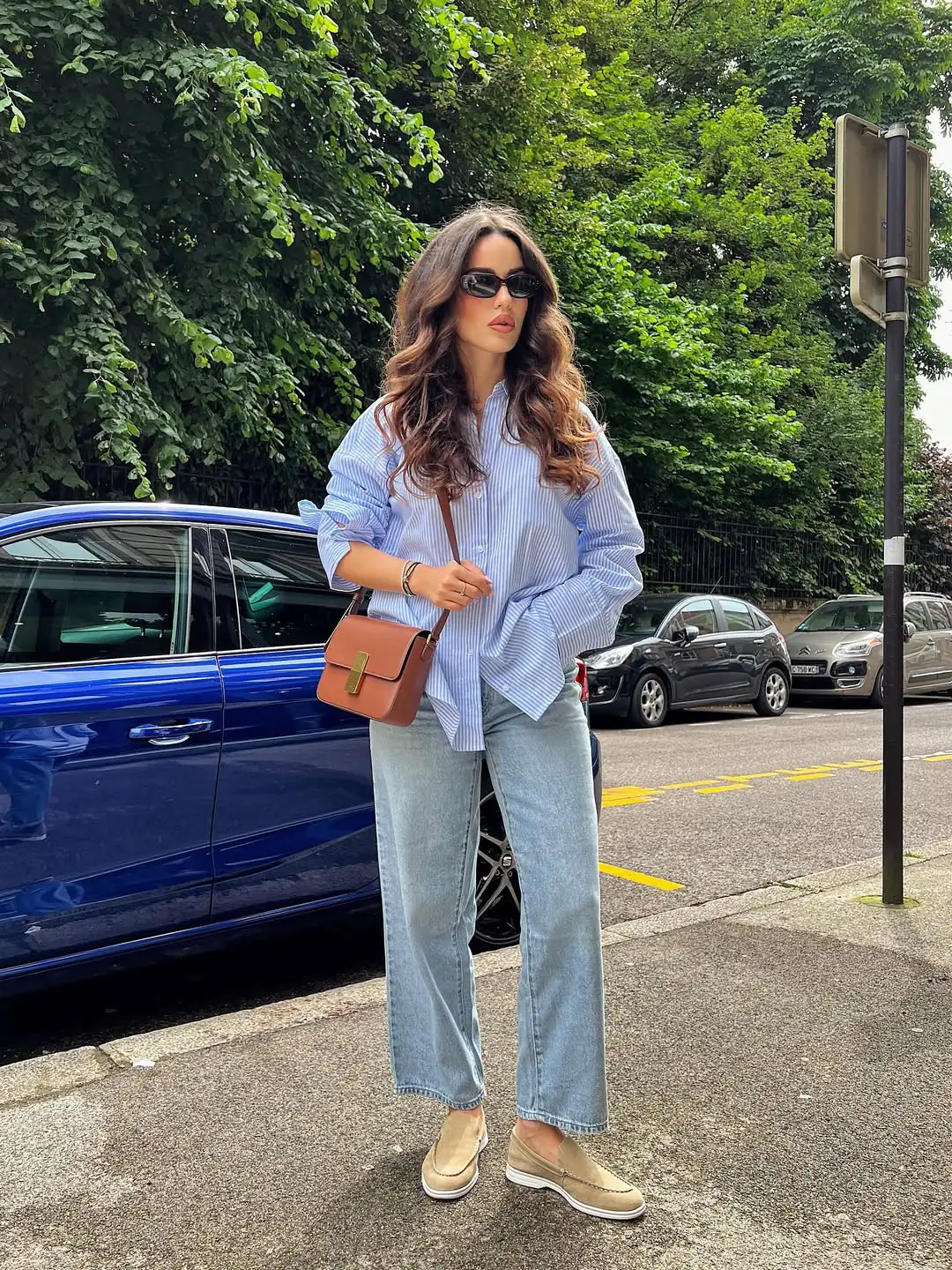 woman wearing blue striped oversized shirt and light wash jeans with tan loafers outdoors