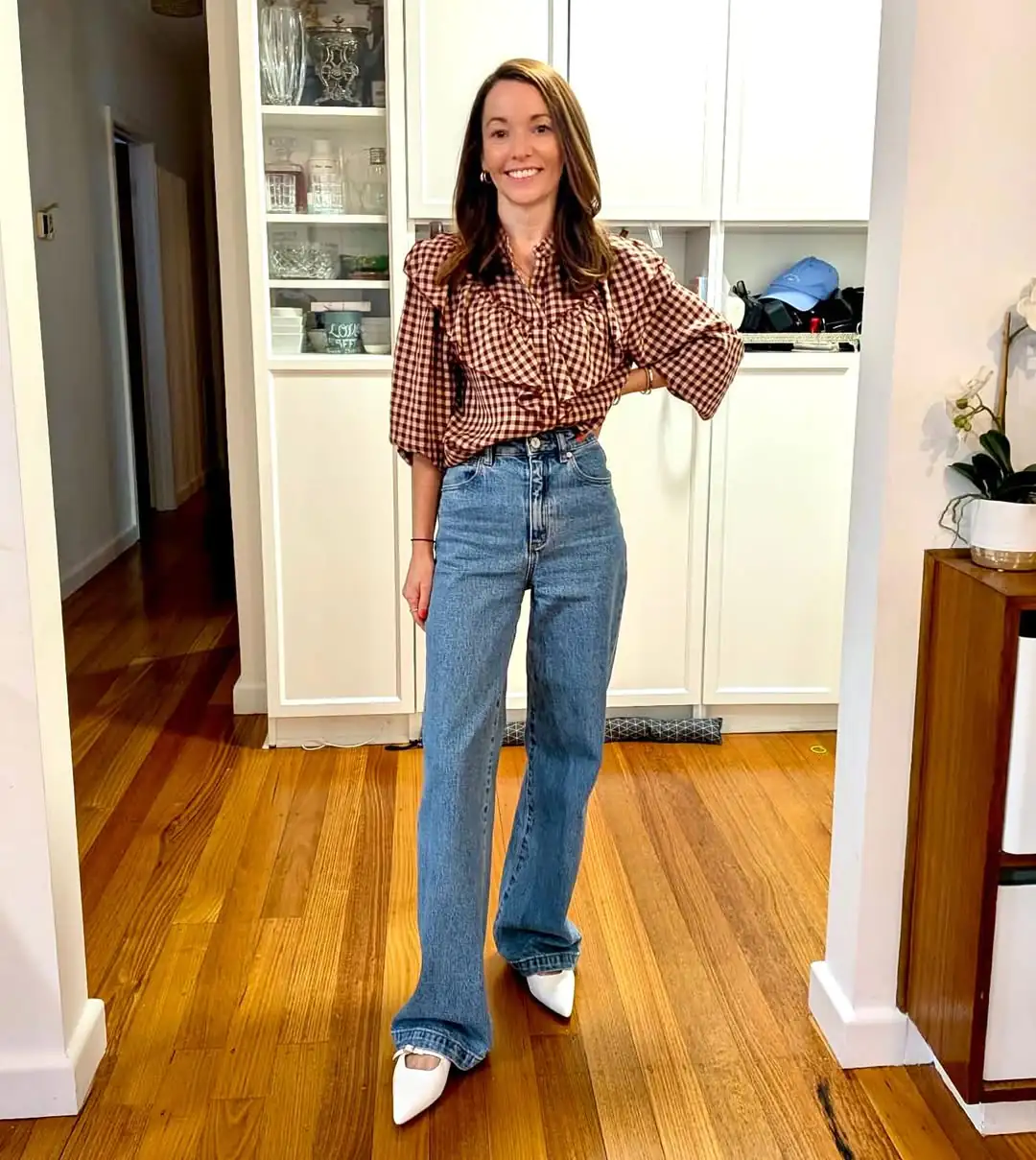 smiling woman wearing gingham ruffle blouse and high waisted straight leg blue jeans