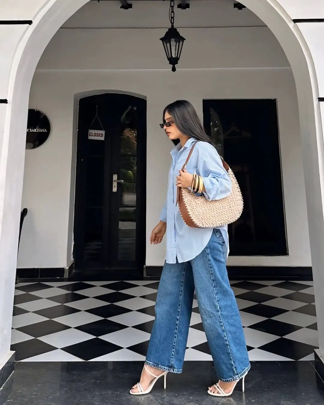 woman in light blue oversized shirt and wide leg jeans walking on checkered floor