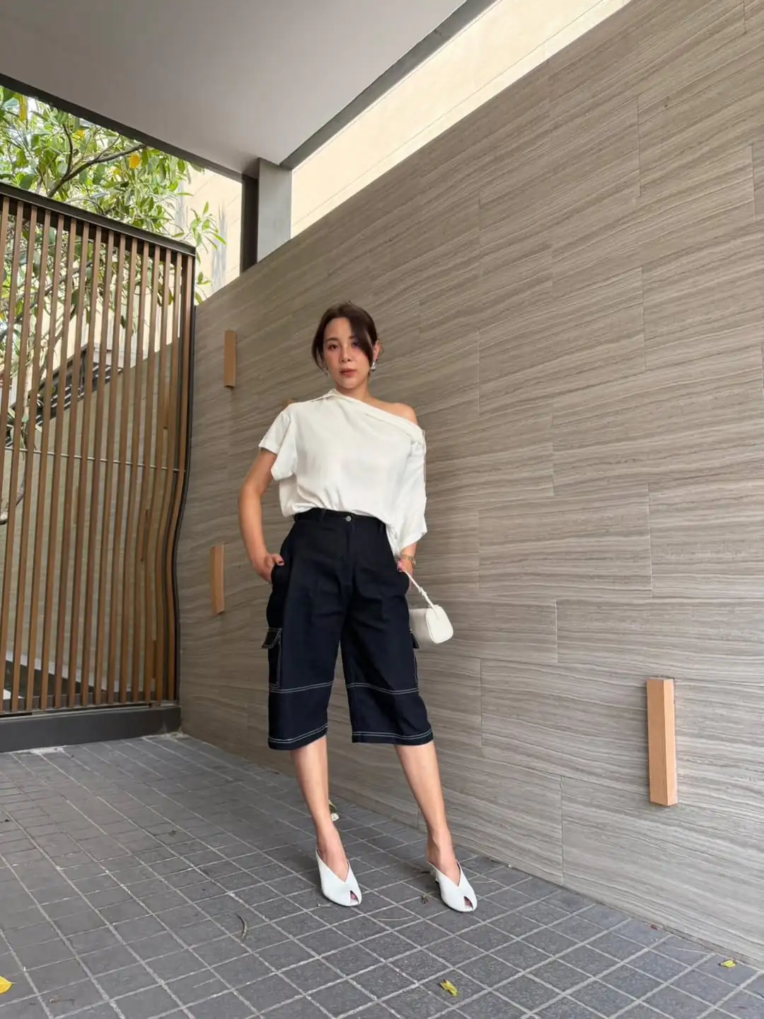 woman in off the shoulder white top and black cargo shorts with white heels