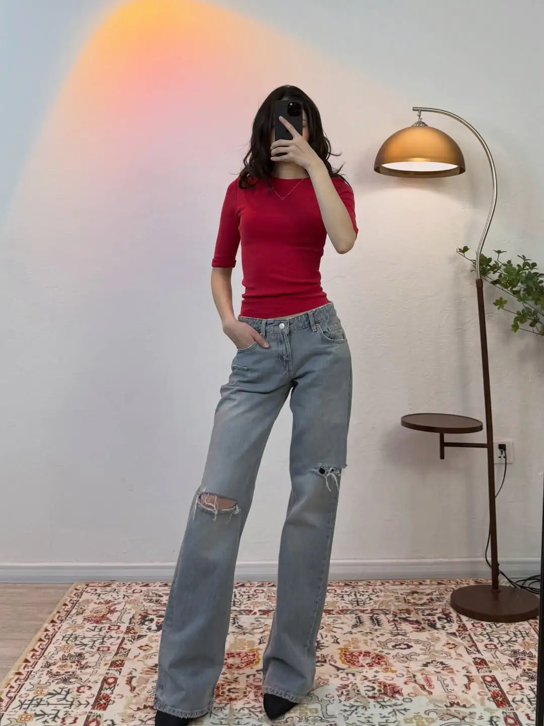 woman in red short sleeve top and ripped light wash jeans taking mirror selfie