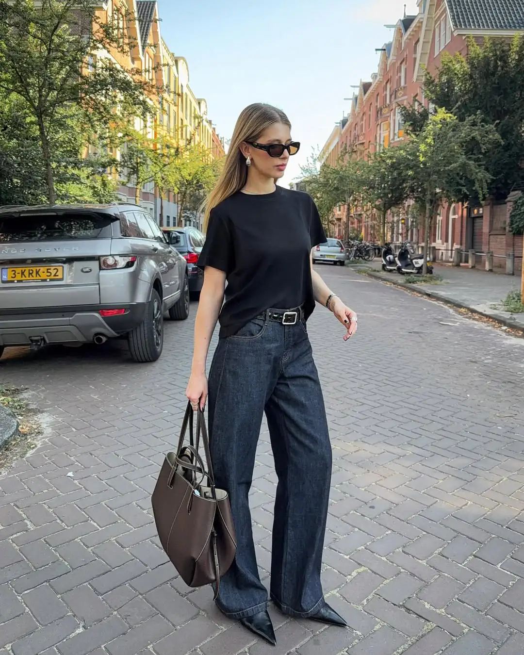 blonde woman in black t-shirt and dark wash wide leg jeans on cobblestone street