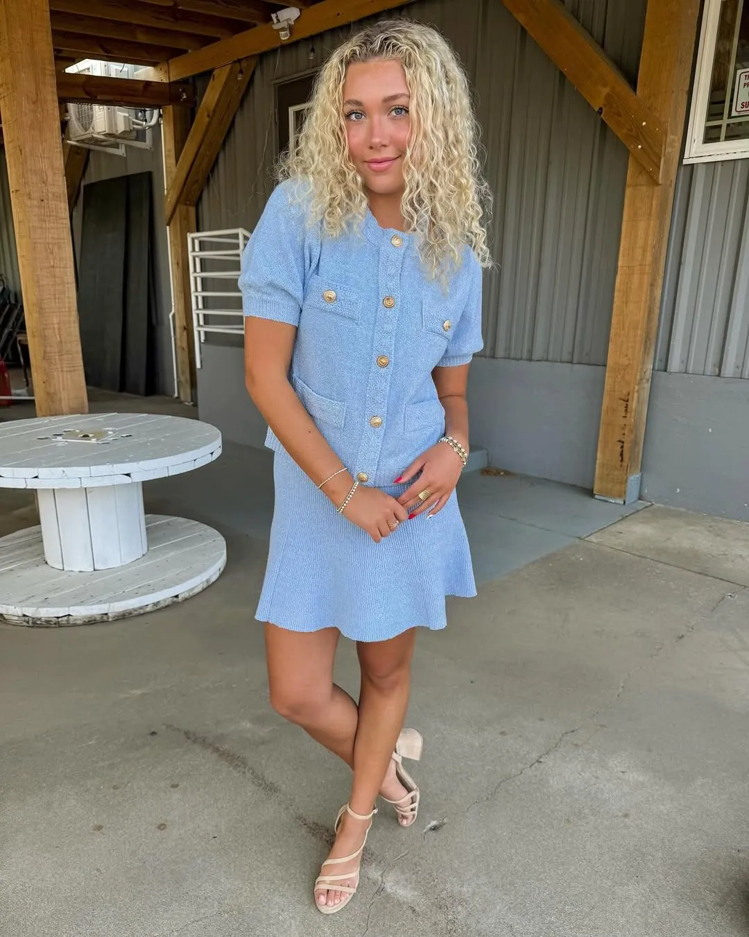woman in light blue short-sleeve cardigan and matching mini skirt with gold buttons.